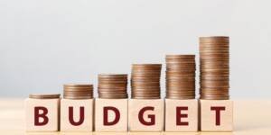image shown Stacked coins increasing in height on wooden blocks spelling BUDGET."
